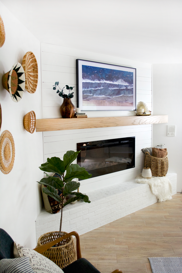 a boho bedroom with baskets on the wall and a white fireplace with the samsung frame